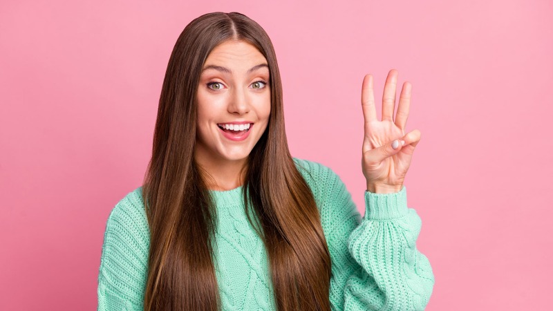 Pink background and a woman holding up three fingers