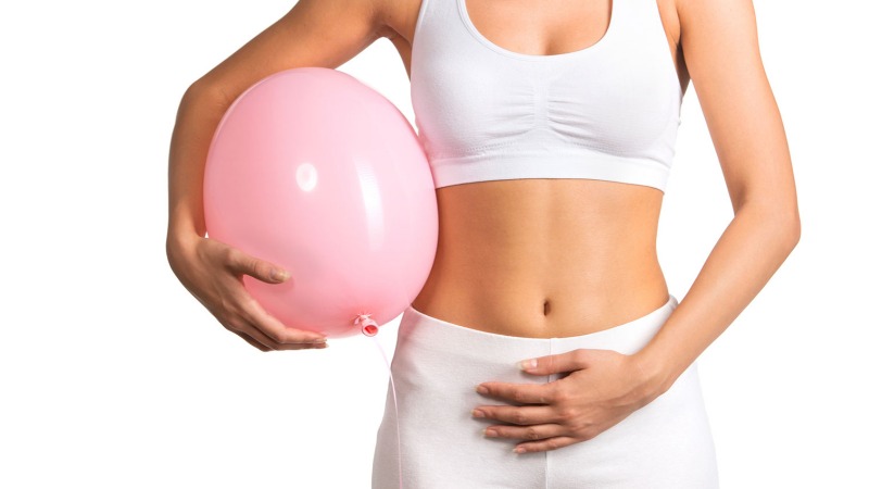 View of a woman's stomach while she is holding a pink balloon